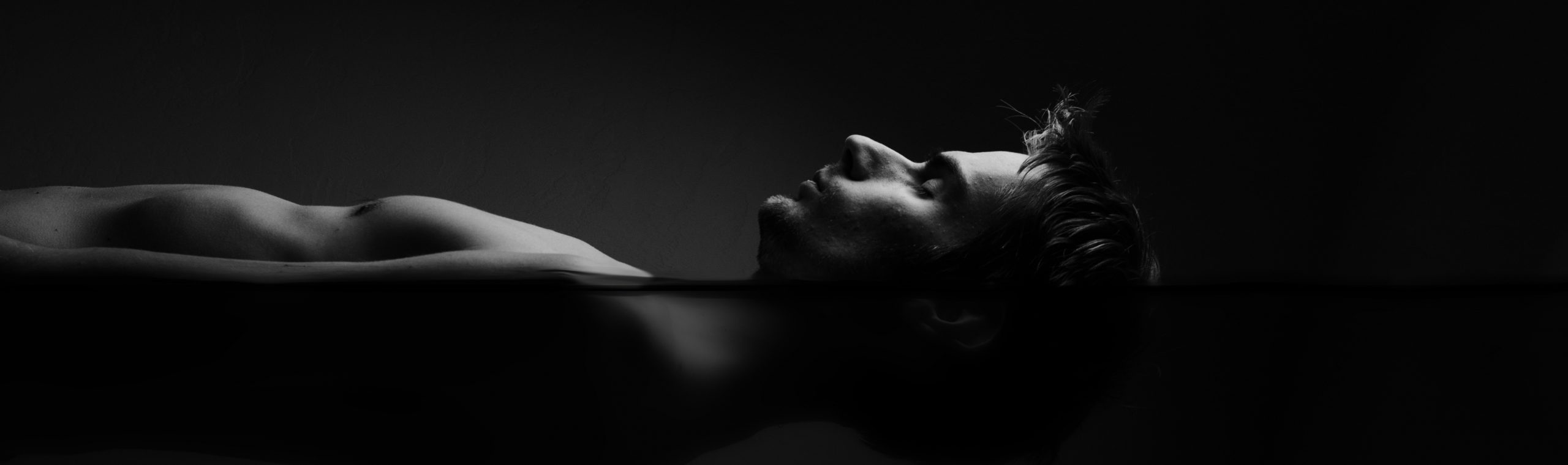 black and white side view of man floating inside sensory deprivation tank