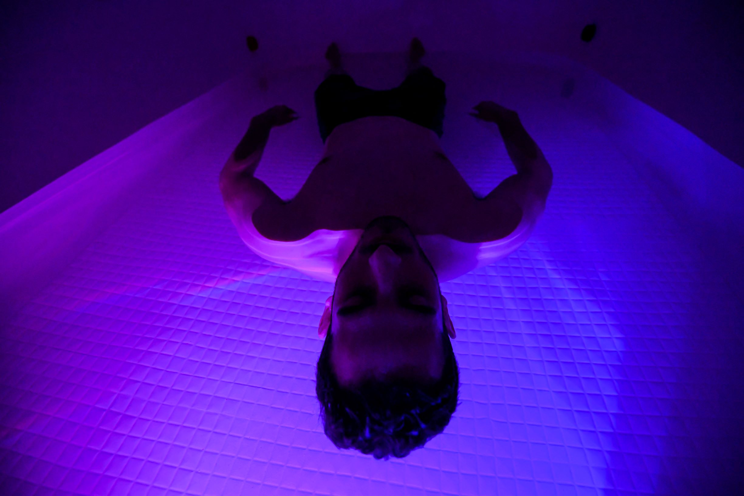 man floating in sensory deprivation cabin with ambient lights on