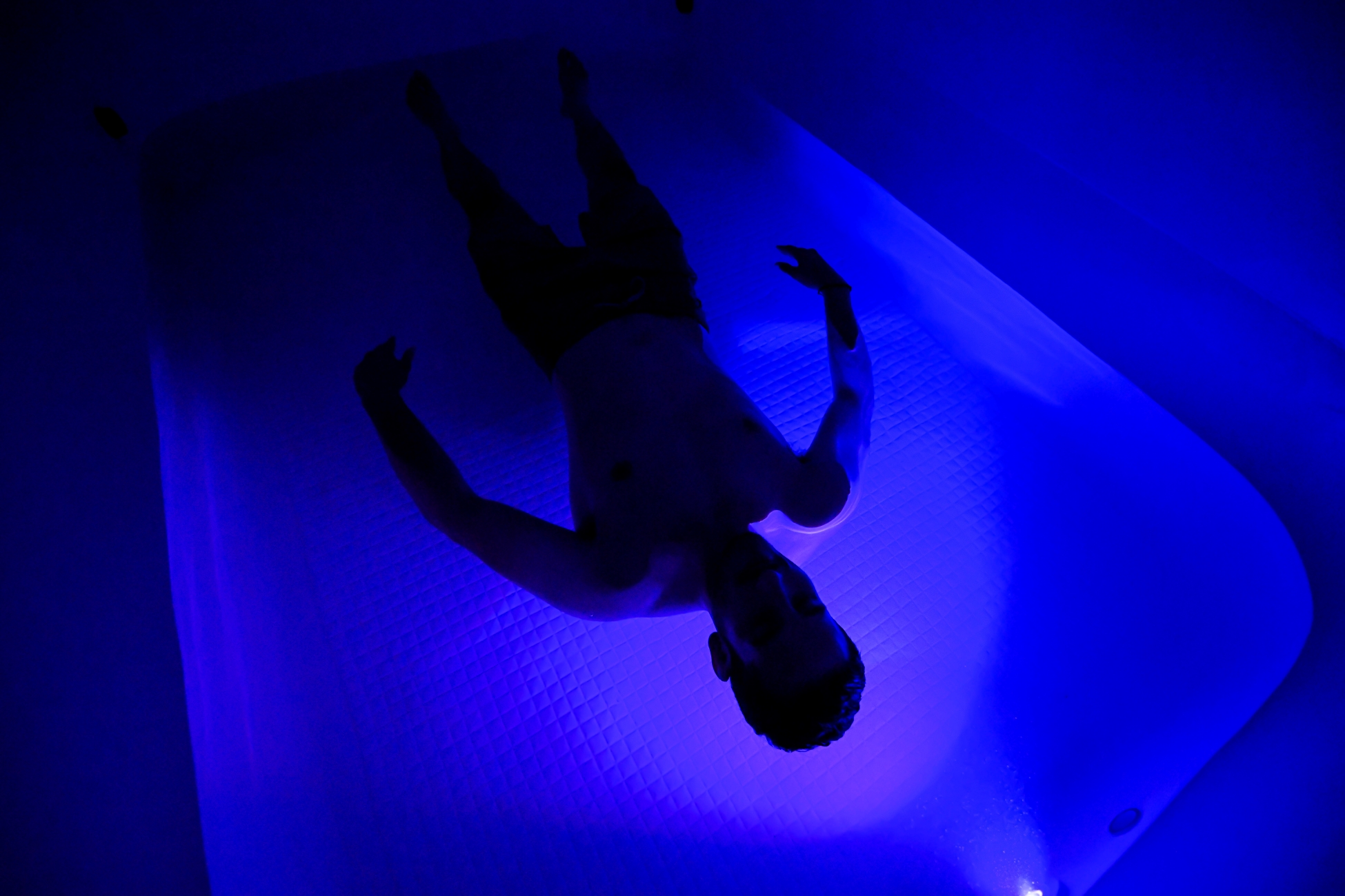 Silhouette of man floating inside large float tank with ambient light on